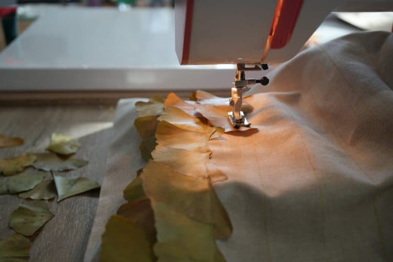 Primer plano de una máquina de coser uniendo hojas de ginkgo sobre una tela beige en un taller artesanal